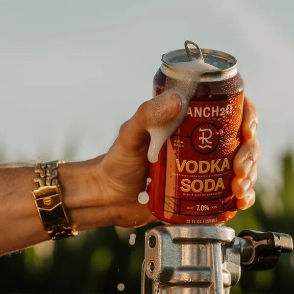 Close-up of a hand holding a foaming can of Rancho Vodka Soda with condensation in the sunlight.