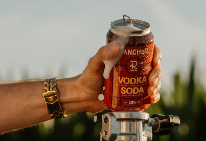 Close-up of a hand holding a foaming can of Rancho Vodka Soda with condensation in the sunlight.