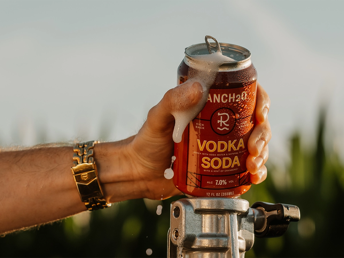 Close-up of a hand holding a foaming can of Rancho Vodka Soda with condensation in the sunlight.