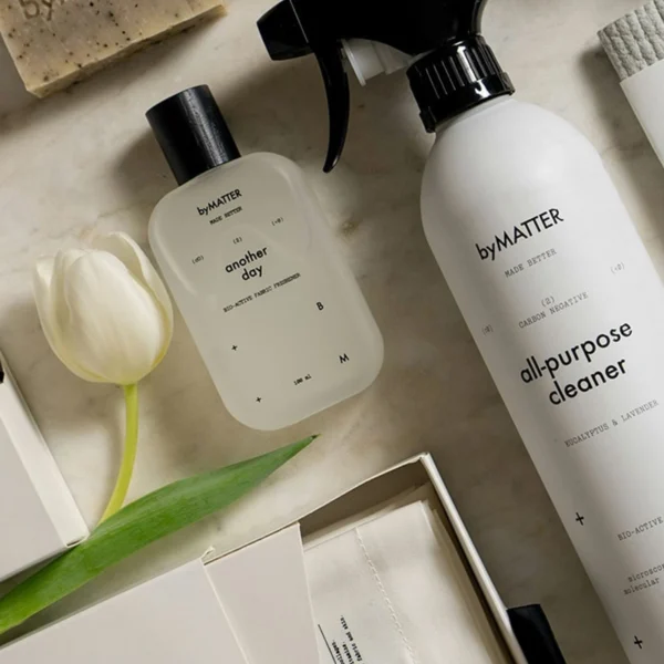 Flat lay of eco-friendly byMATTER cleaning products including all-purpose cleaner, soap, cloths, and minimalist packaging with white tulips.