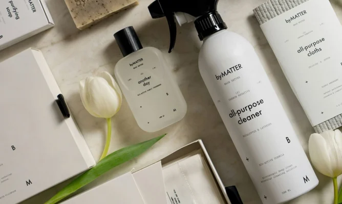 Flat lay of eco-friendly byMATTER cleaning products including all-purpose cleaner, soap, cloths, and minimalist packaging with white tulips.