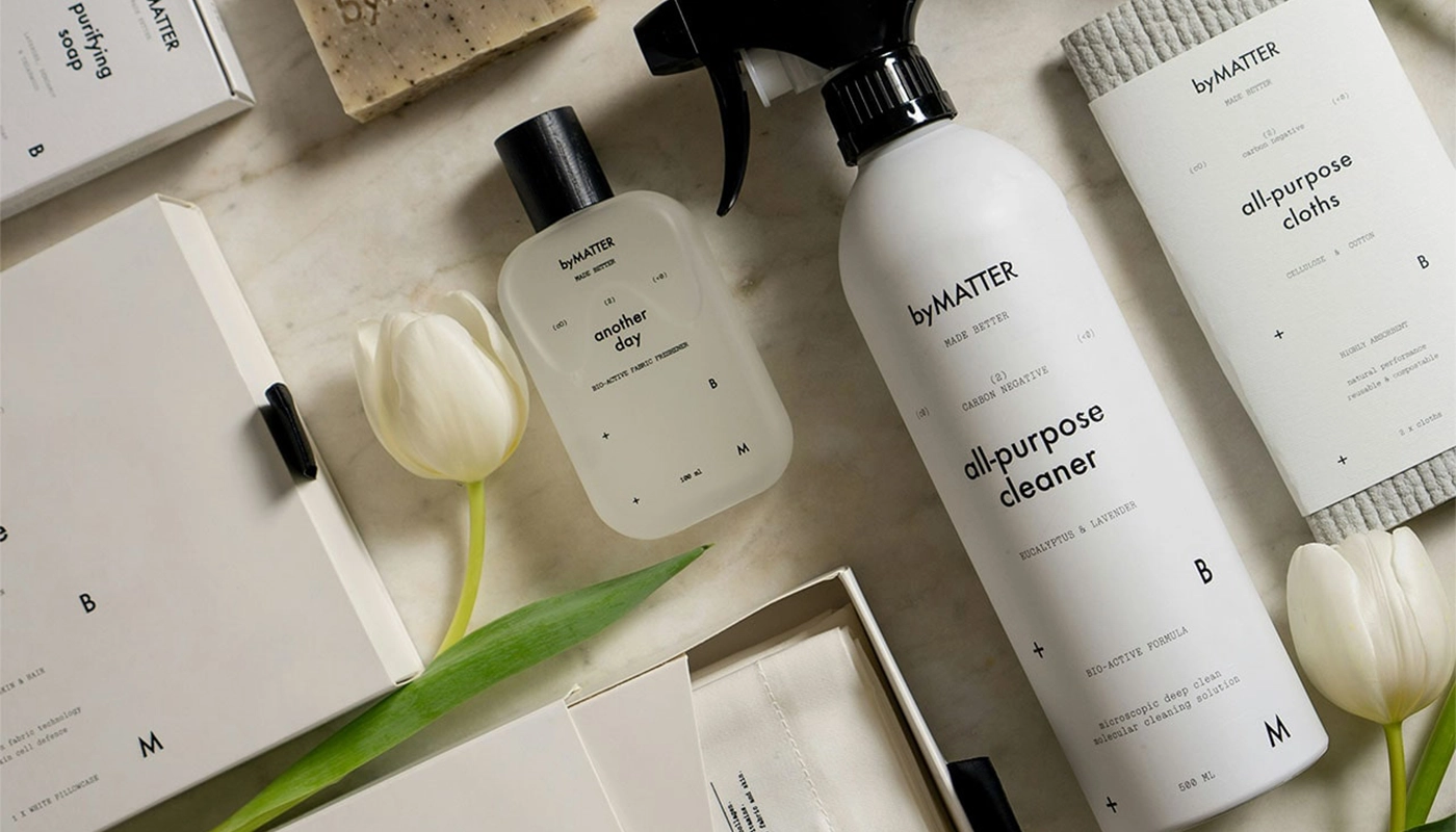 Flat lay of eco-friendly byMATTER cleaning products including all-purpose cleaner, soap, cloths, and minimalist packaging with white tulips.