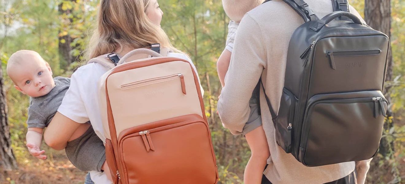 Parents carrying babies and wearing MAPAII diaper backpacks in neutral and black while walking outdoors.