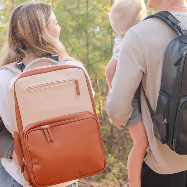 Parents carrying babies and wearing MAPAII diaper backpacks in neutral and black while walking outdoors.