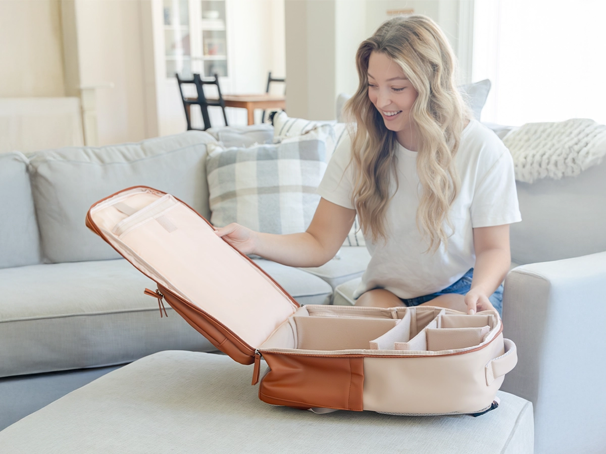 Smiling woman sitting on a couch opening a MAPAII diaper backpack to reveal its spacious and organized compartments.
