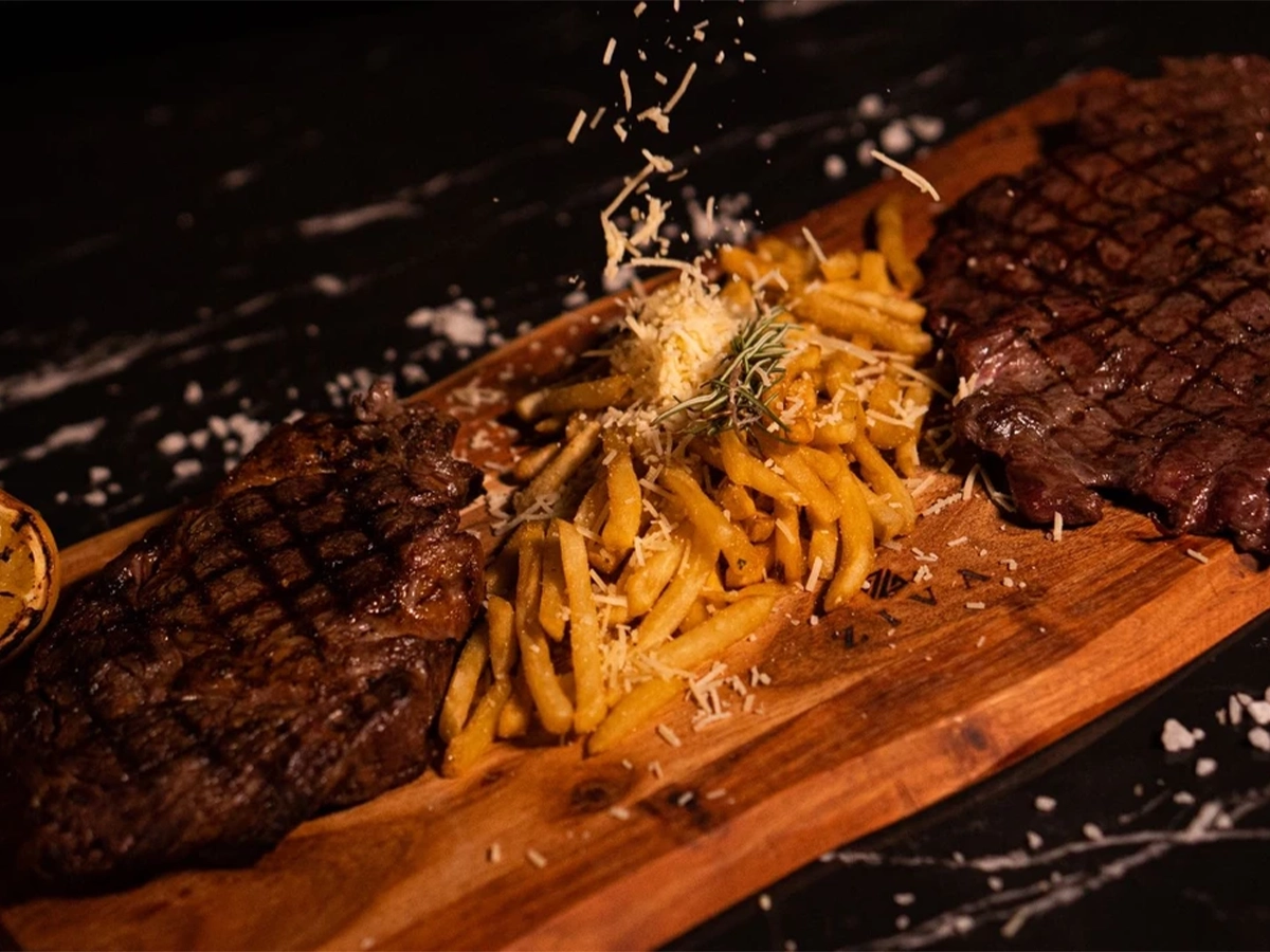 Juicy grilled steaks served with golden fries topped with grated cheese on a wooden board.