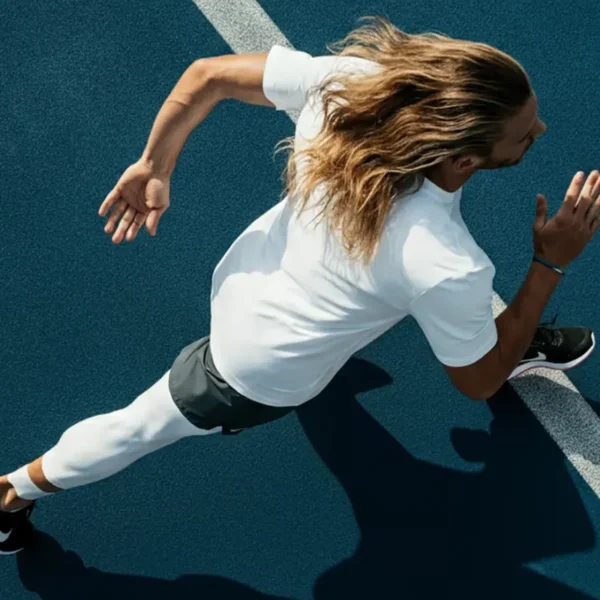 Athlete with long hair sprinting on a blue running track, captured from above in mid-stride.