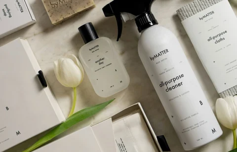 Flat lay of byMATTER eco-friendly products including all-purpose cleaner, another day fragrance, cleansing cloths, and natural soap with minimalist packaging.